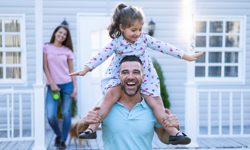 Dad with his daugther on his shoulder and wife looking on from the deck