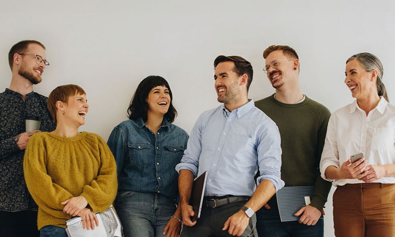 Five coworkers smiling in the office together against a gray wall.