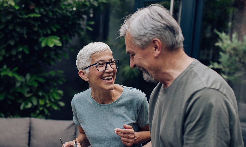 Retiree couple smiling at each other outside in their backyard.