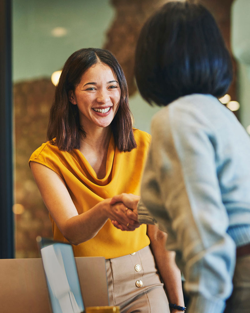 Two women in an office, shaking hands when meeting.